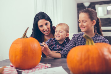 Fototapeta na wymiar Mother with daughter and son creating big orange pumpkin for Halloween