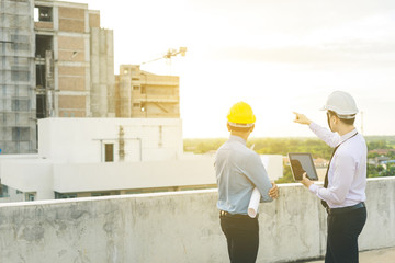 smiling young architect or engineering builder in hard hat with tablet over group of builders at...