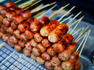 Grilled Thai local traditional street stall food fermented sour pork and rice sausage stick piled on black iron mesh, on aluminum tray in night market