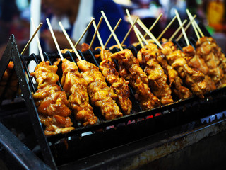 Raw chicken meat stick grilling on charcoal oven with soy seasoning sauce, on street food stall cart in night market, as Thai local traditional