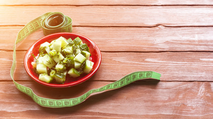.Fresh cucumber salad and measuring tape on a colored background concept diet