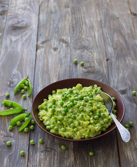 Mashed potatoes with green peas, mint and olive oil in a ceramic bowl on a wooden table with free space. Healthy vegetarian food