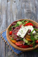 Homemade Greek salad from tomatoes, cucumbers, sweet peppers, cheese, olives and greens in a wooden bowl on a wooden table with free space. Healthy delicious food