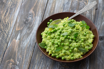 Mashed potatoes with green peas, mint and olive oil in a ceramic bowl on a wooden table with free space. Healthy vegetarian food