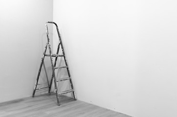 Black-and-white photograph of a ladder to repair a stained white paint standing in the corner of a freshly painted room on the new floor.