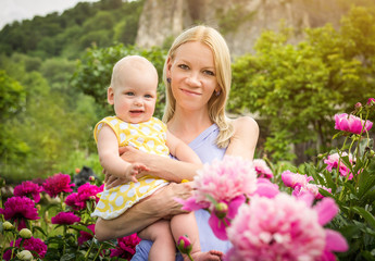 Happy woman and child in the blooming peony flowers
