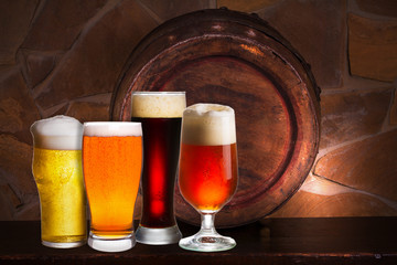 Set of various glasses of beer in cellar, pub or restaurant. Beer glasses, old beer barrel and brick wall on background. Still life with ale