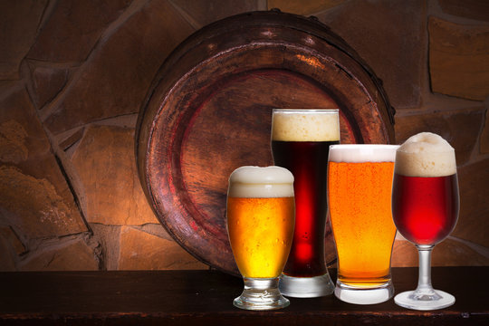 Set of various glasses of beer in cellar, pub or restaurant. Beer glasses, old beer barrel and brick wall on background. Still life with ale