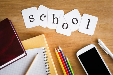 Inscription school with supplies and mobile phone on the student table. Top view. Education concept. 