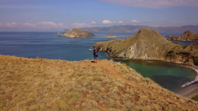 Beautiful aerial landscape footage of a young woman enjoying freedom by standing on the Padar Island hill at East Nusa Tenggara, Indonesia. Shot in 4k resolution
