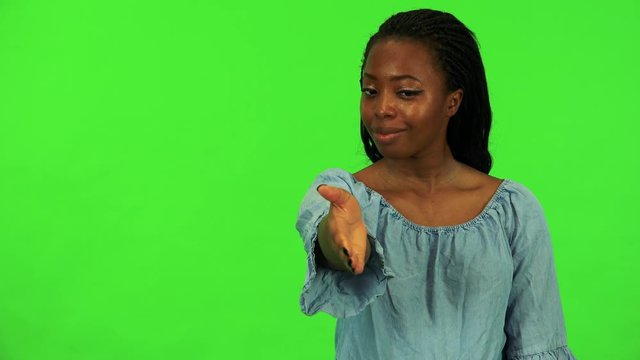 A young black woman extends her arm to the camera for a handshake - green screen studio