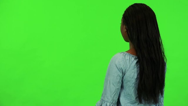A young black woman with her back to the camera looks around - green screen studio