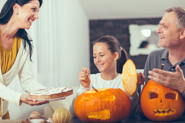 Family are celebrating Halloween. They are sitting at the table with pumpkin