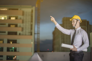 Smiling young architect or engineering builder in hard hat with tablet over group of builders at...