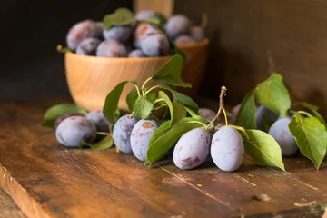 Foto op Plexiglas Fresh plums with green leaves in wooden pot on the dark wooden table. Shallow depth of field. Toned. © Victoria Kondysenko