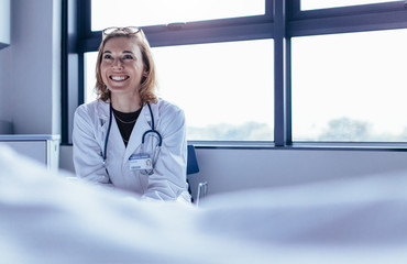 Happy female doctor sitting in hospital room - Powered by Adobe