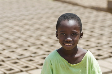 Little African child smiling outdoors behind bricks - Child Labour concept