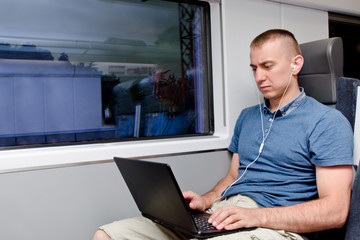 Young man working behind a laptop sitting in a train chair