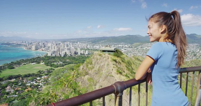 Happy hiker enjoying view of Waikiki Beach and Honolulu city. Smiling young woman is standing on observation point at Diamond Head State Monument during summer. Oahu, Hawaii, USA.