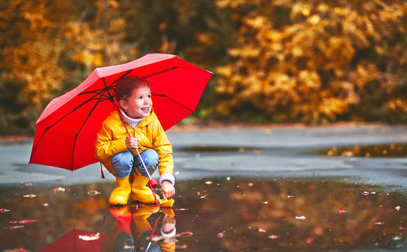 happy child girl with umbrella and paper boat in   puddle in   autumn on nature