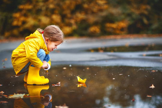 happy child girl with paper boat in   puddle in   autumn on nature.