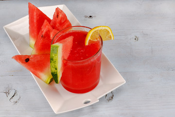 Watermelon smothie and slices with lemon on wood background