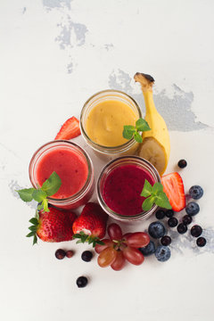 Assortment of bright fruit and berry smoothies on white table. Summer refreshing drinks. Space for text