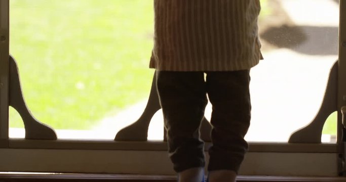Toddler boy looks through screen door on tippy toes - tilt down