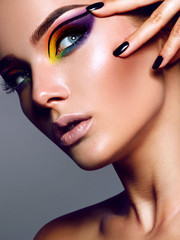 Fototapeta premium A beautiful sexy young girl with tanned smooth skin and a bright colored make-up in the studio on a gray background holds her hand near the face with painted black nails.