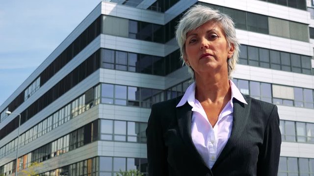 Business middle age woman looks to camera with serious face as boss - company building in the background 