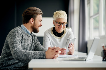 Businessman sitting and looking at tablet device while colleague showing him web site