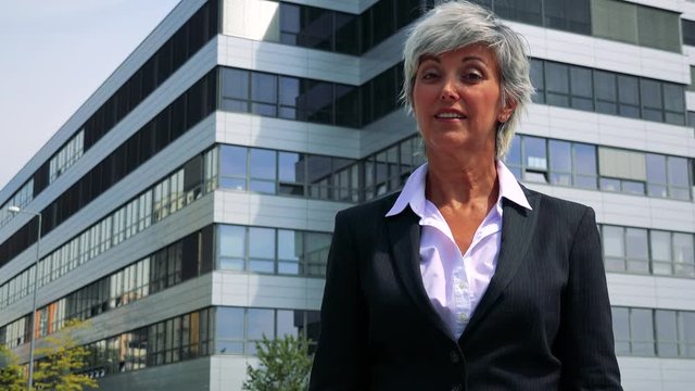 Business middle age woman agrees and shakes with head - company building in the background 