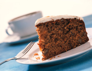 Carrot cake on white plate with cup of coffee in background