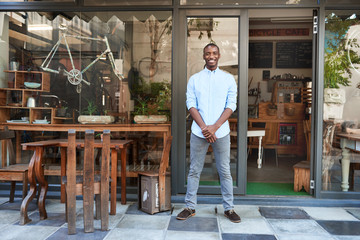 Smiling African entrepreneur standing welcomingly in front of his cafe