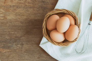 Fresh eggs in old wood basket put on white napkin. Prepare chicken eggs and egg whisk for cooking or bakery on rustic wood table.Top view, flat lay of eggs with copy space for background or wallpaper.