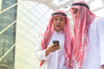 Closed up of Two Arabian Muslim businessman standing  in city ,outdoor office discussing work with cell-phone. Ethnic business people in urban concept.