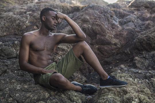 Photo shoot for a black handsome guy on the rocky shore of the ocean