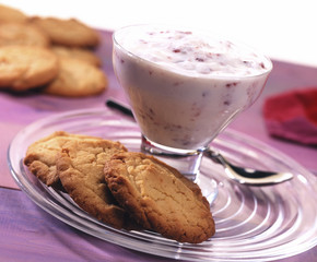Strawberry yoghurt in glass bowl served on plate with fresh biscuits  