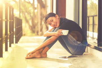 Fototapeta na wymiar Asian woman smiling happy drinking coffee in sun sitting outdoor home in sunshine light enjoying her morning coffee. vintage toned