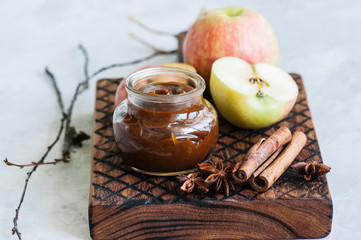 Ingredients for traditional apple pie- salted caramel, slices of apple in caramel sauce, cinnamon sticks on a wooden board. White stone background and close up.