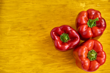 Three red bell pepper close up on wooden yellow background with copy space on the left side. Bell peppers on wooden yellow texture close up. Top view