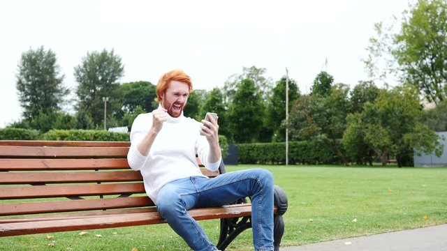 Man Excited for Successs, Using Smartphone, Sitting on Bench