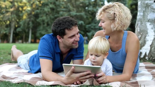 Happy family with baby enjoying a tablet computer in the park. Family and modern technology.