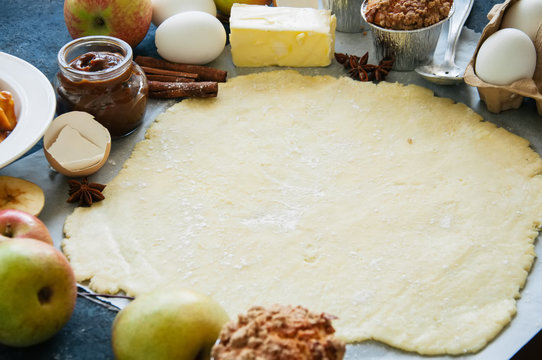 Group of ingredients for baking, raw dough for pie, spices, apples, caramel, eggs and butter on a blue table. Top view and copy space.