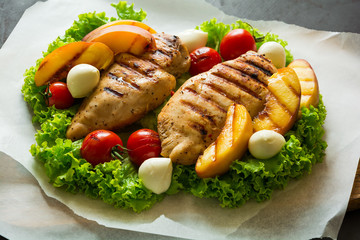 BBQ: grilled chicken breast, tomatoes,peach slices and mini mozzarella on wooden desk. Vibrant colors