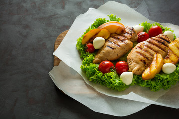 BBQ: grilled chicken breast, tomatoes,peach slices and mini mozzarella on wooden desk. Vibrant...