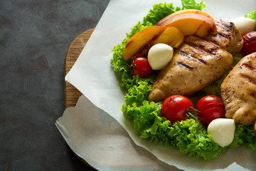 BBQ: grilled chicken breast, tomatoes,peach slices and mini mozzarella on wooden desk. Vibrant colors