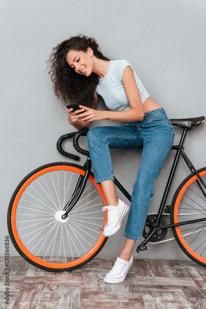 Sticker Full length image of smiling curly woman sitting on bicycle