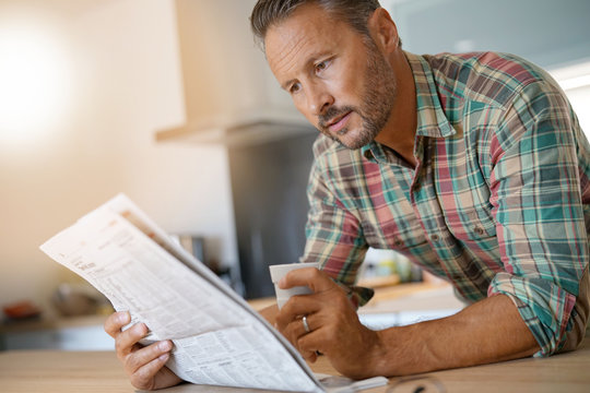 Smiling mature man drinking coffee and reading newspaper