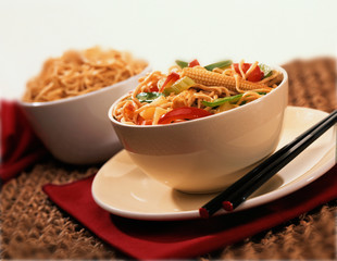 Vegetable stir fry in white bowl with black chopsticks and bowl of noodles in background